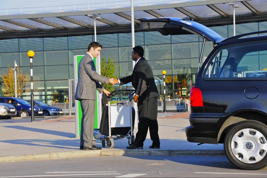 Driver meeting a traveller beside an airport transfer vehicle