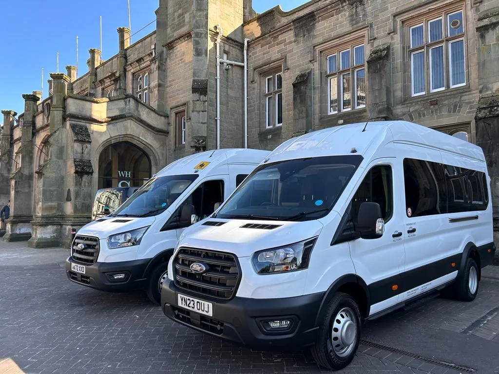 Two white passenger minibuses parked outside a building